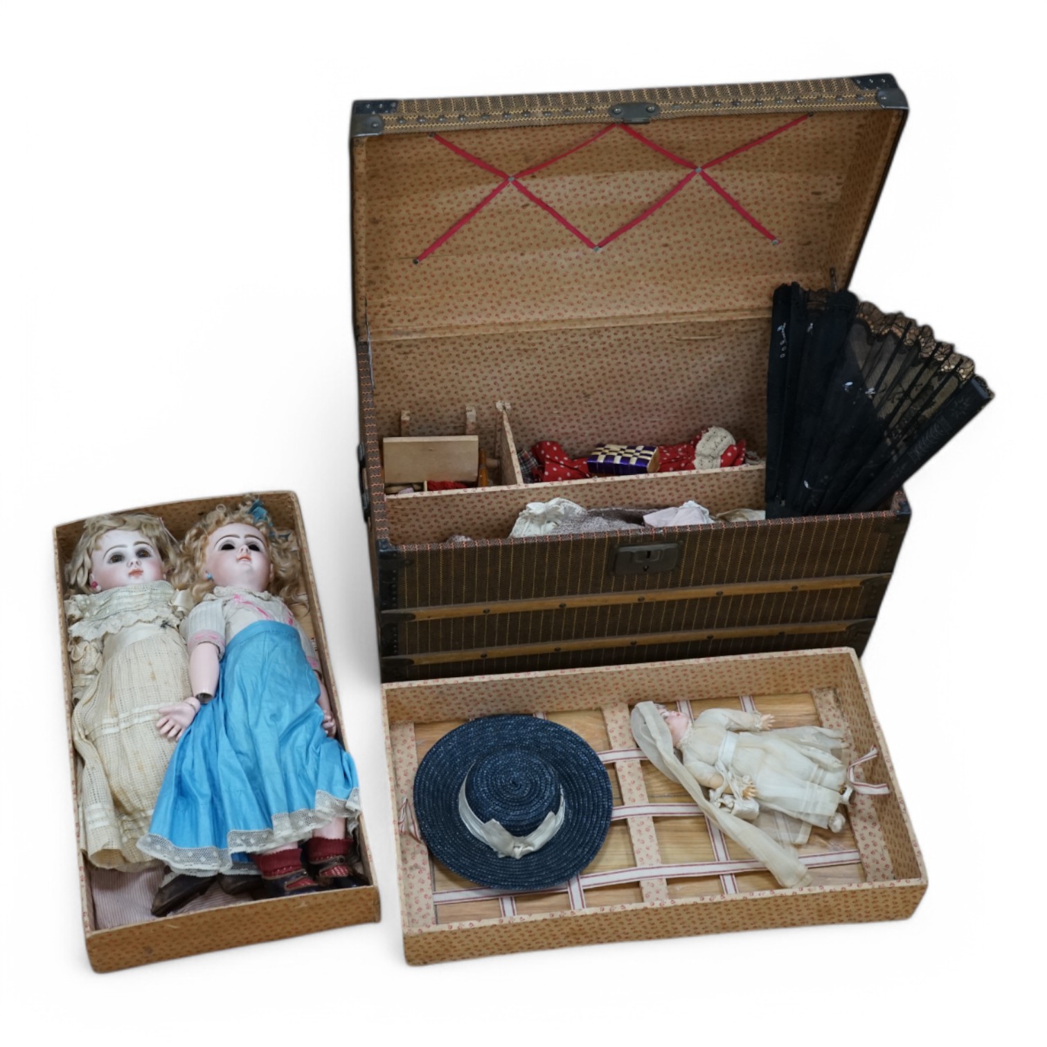 A Tête Jumeau bisque doll, closed mouth and paperweight eyes, jointed wood and composition body, two other French bisque dolls and assorted clothing, all contained within a three-layer wood and metal-bound cabin trunk, J